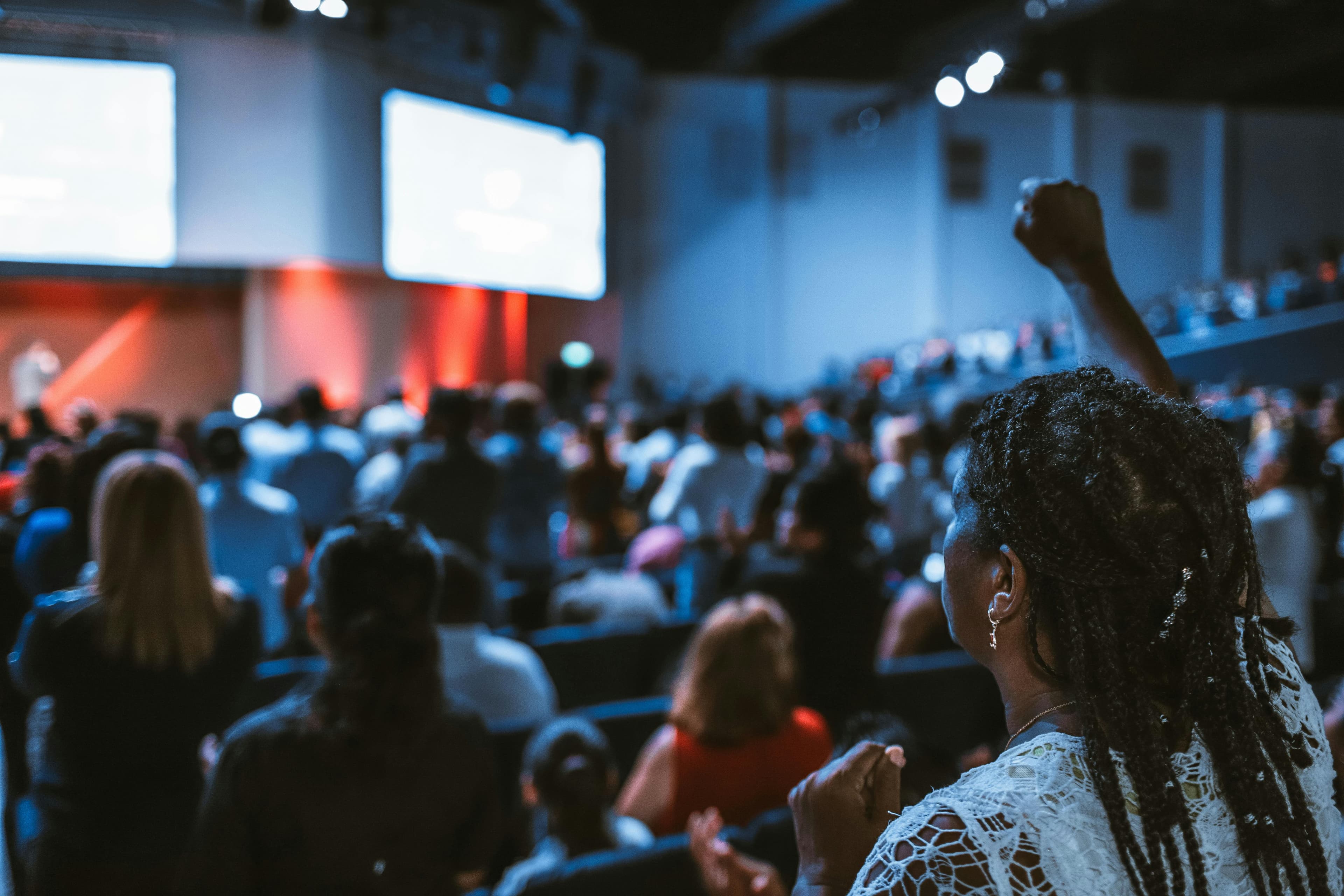 Representational image of conference with a woman raising a hand to ask question